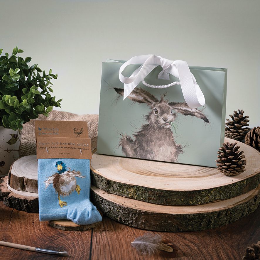Gift bag with a rabbit design on a wooden surface with a plant and pinecones.