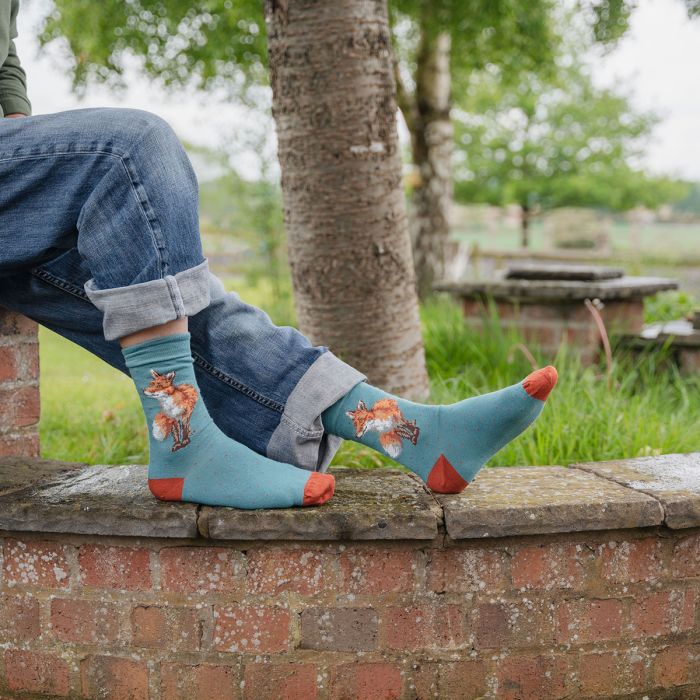 Person wearing blue socks with fox designs sitting on a brick wall outdoors.