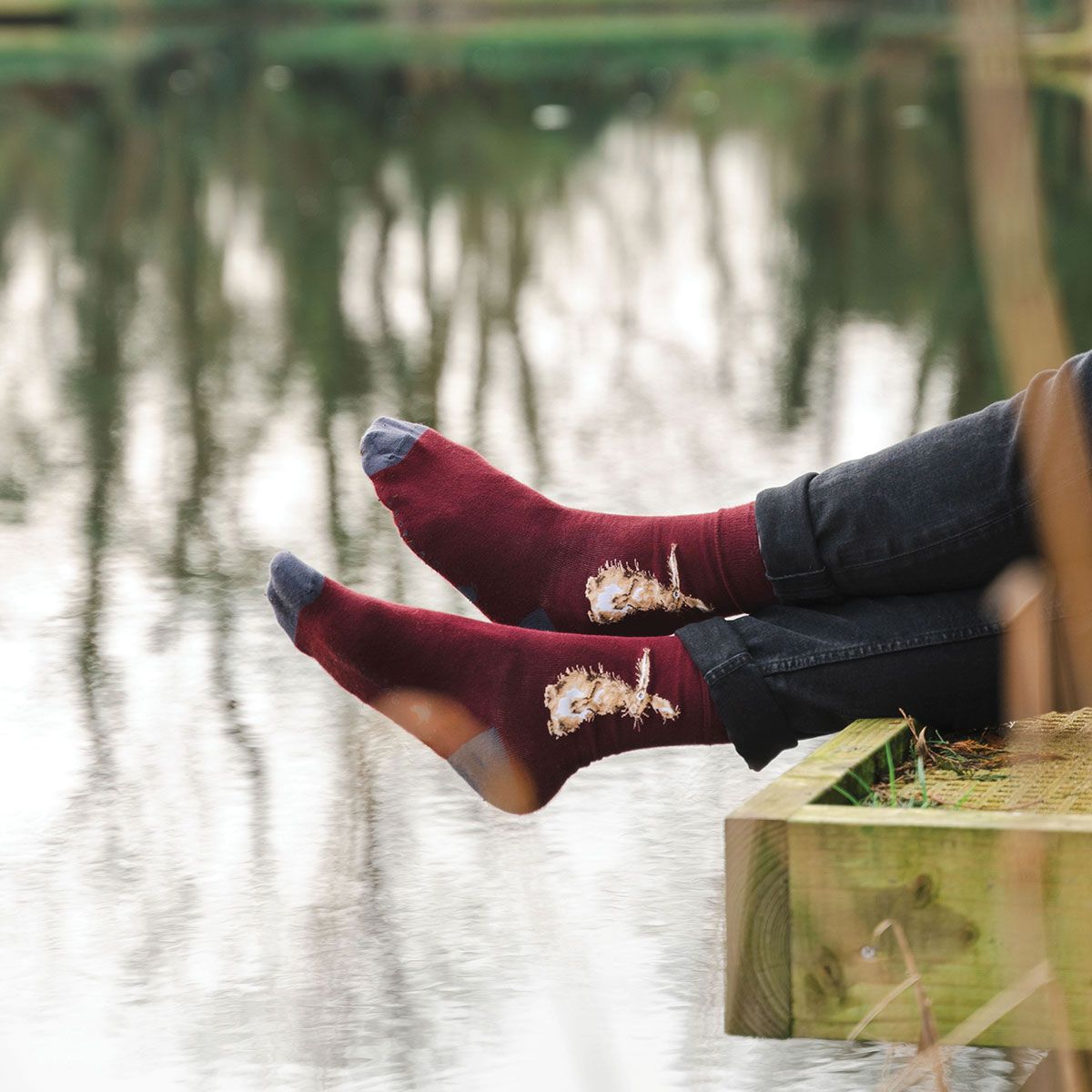 Person wearing maroon socks with a nature design, sitting by a body of water.
