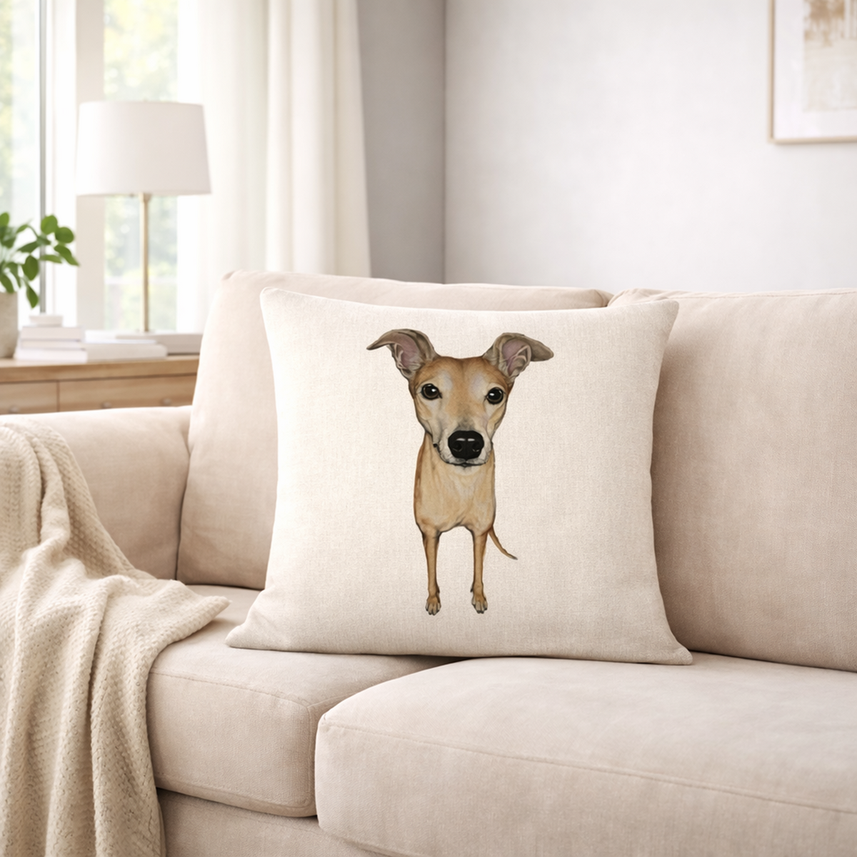 A square cream cushion cover  featuring a printed illustration of a light brown greyhound whippet dog, styled on a beige sofa in a bright, modern living room.