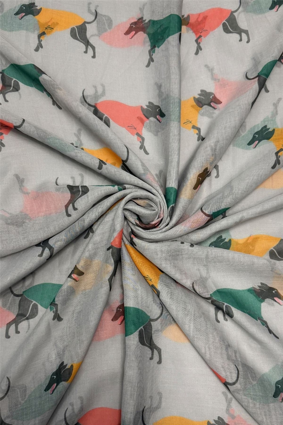 Light grey fabric printed with a repeating pattern of greyhound dogs wearing colourful shirts in green, orange, yellow, and pink, arranged in a spiral drape.