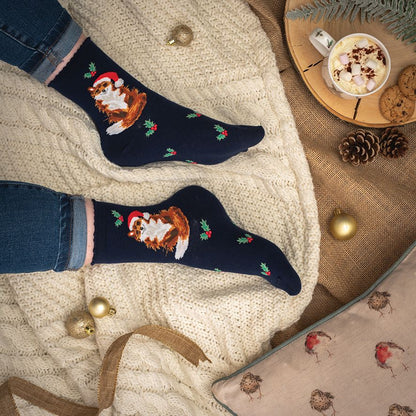 Navy blue socks with festive designs worn by a person, placed on a textured surface with a cup of hot chocolate and cookies.