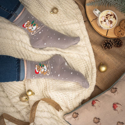 Person wearing festive socks with a Christmas design, surrounded by holiday decor including a mug of hot chocolate and cookies.
