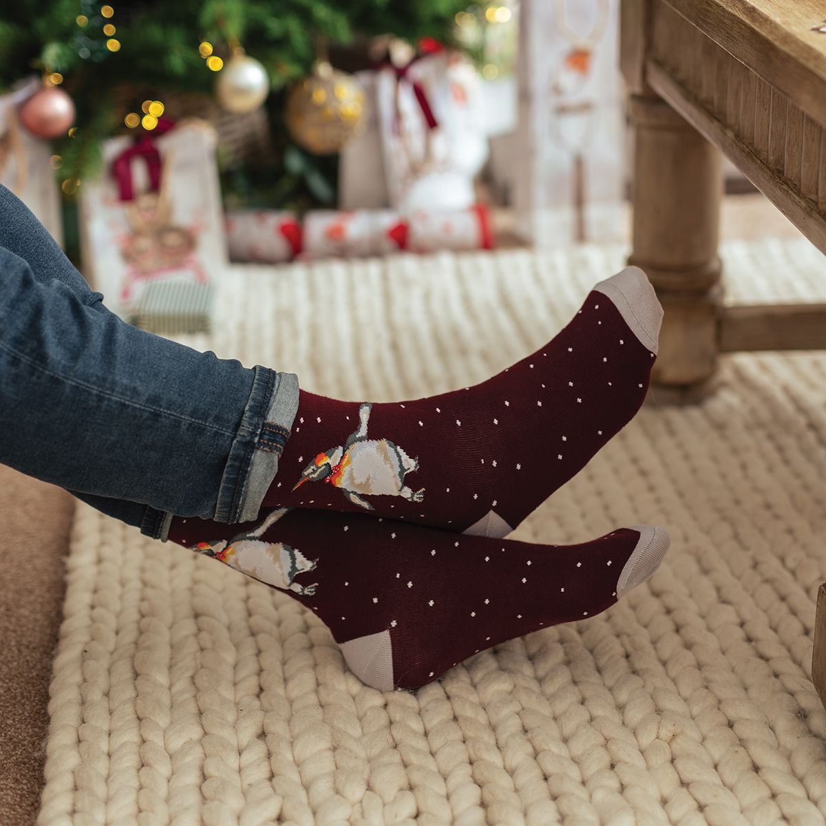 Person wearing festive socks with a Christmas tree and presents in the background